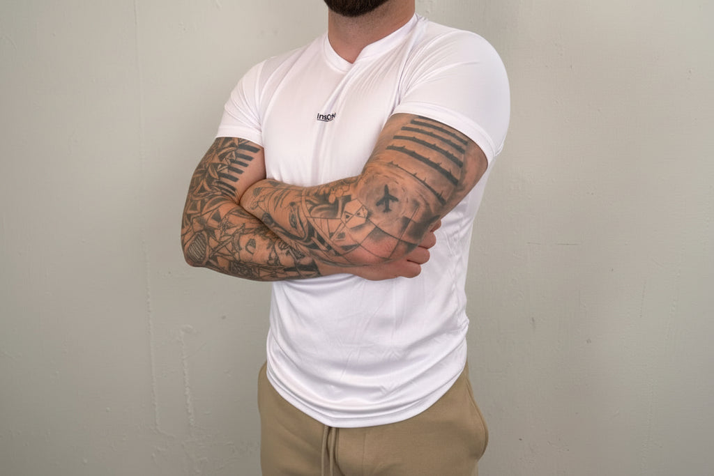 Man wearing a white t-shirt with visible tattoos on his arms against a plain background