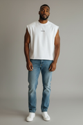 Man wearing a white sleeveless shirt, blue jeans, and white sneakers against a plain background